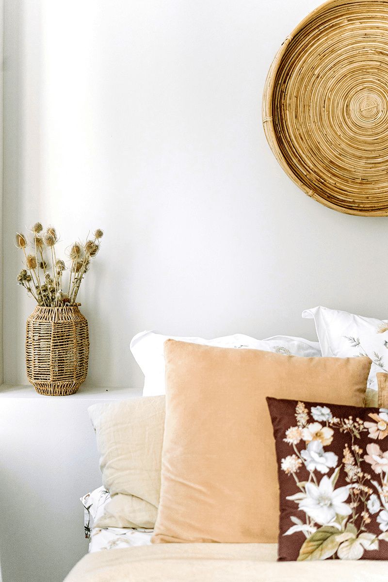 Detailaufnahme einer Wand aus Lehmfeinputz X-WHITE  an der ein Bastkorb hängt und vor der ein Bett mit verschiedenen Kissen steht
