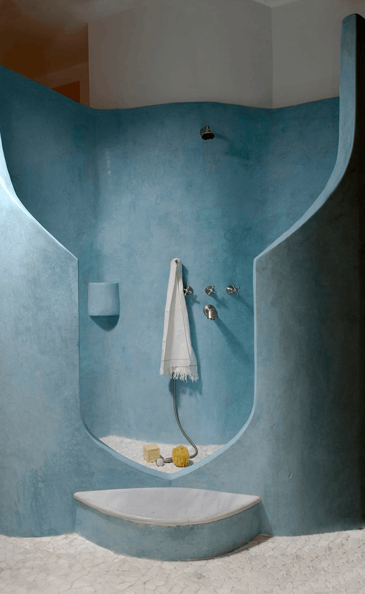 Dusche mit geschwungenem Eingang und einer Tadelakt Stone Oberfläche in Kobalt Blau an deren Duschkopf ein weißes Handtuch hängt