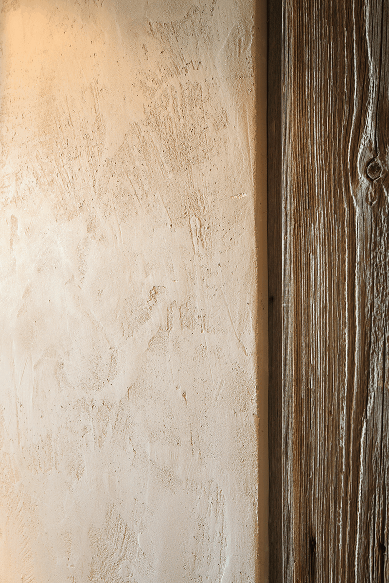 Detailfoto einer Wand die mit Lehmedelputz FINISH verputzt wurde  und auf der sowohl eine Kate zu einem Holztürrahmen  als auch eine leichte Struktur zu erkennen ist