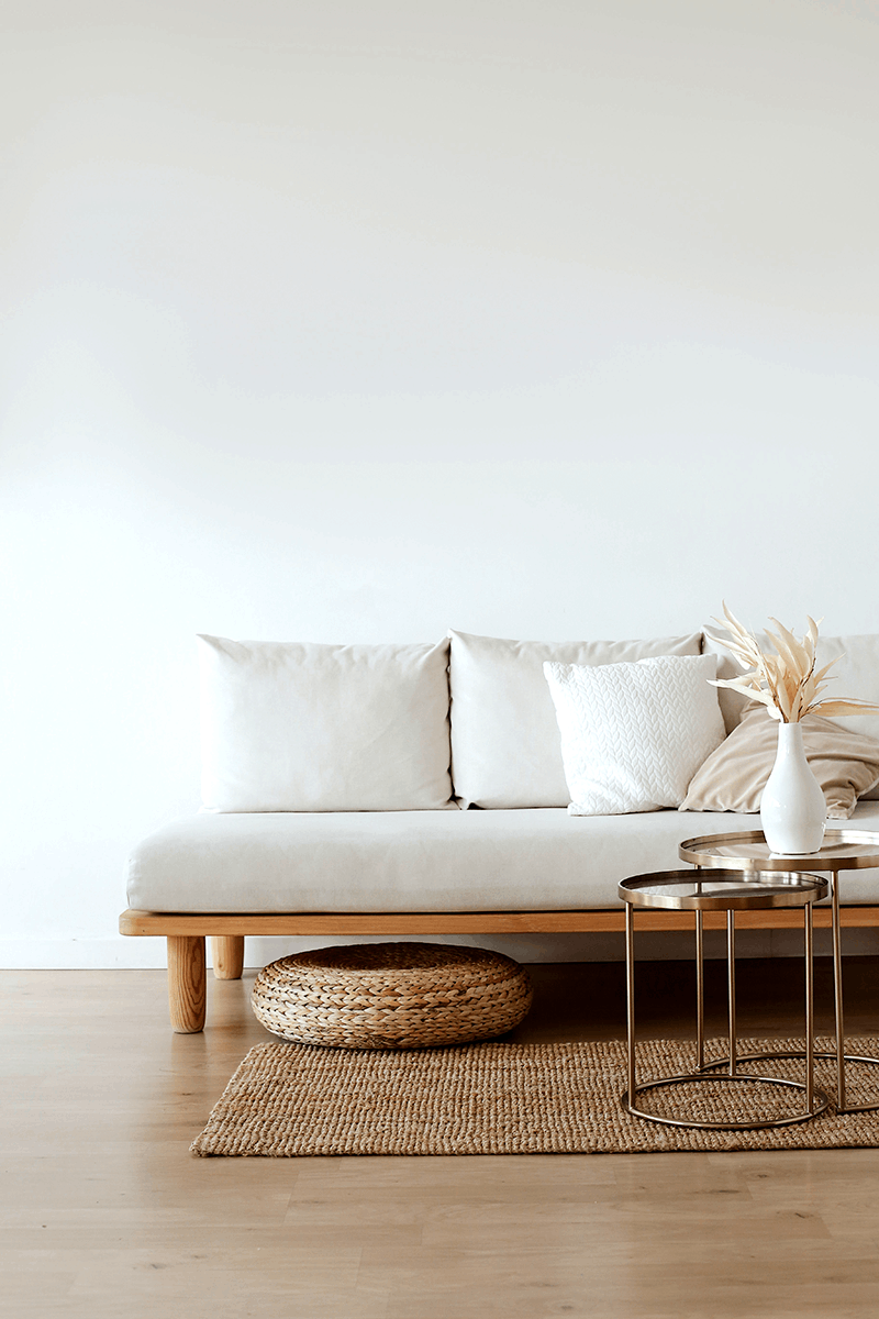 Aufnahme einer weißen Wand aus Lehmfeinputz X-WHITE vor der ein brauner Teppich liegt auf dem ein Sofa in weiß sowie ein Beistelltisch auf Metall steht