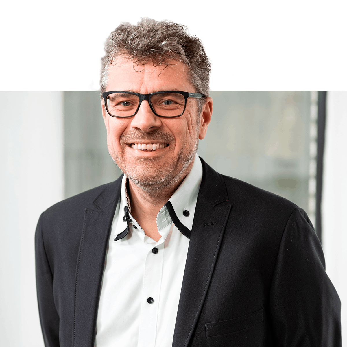 Close-Up Portrait von Ralf Angerstein in die Kamera lachend, mit schwarzer Brille und schwarzem Sakko.