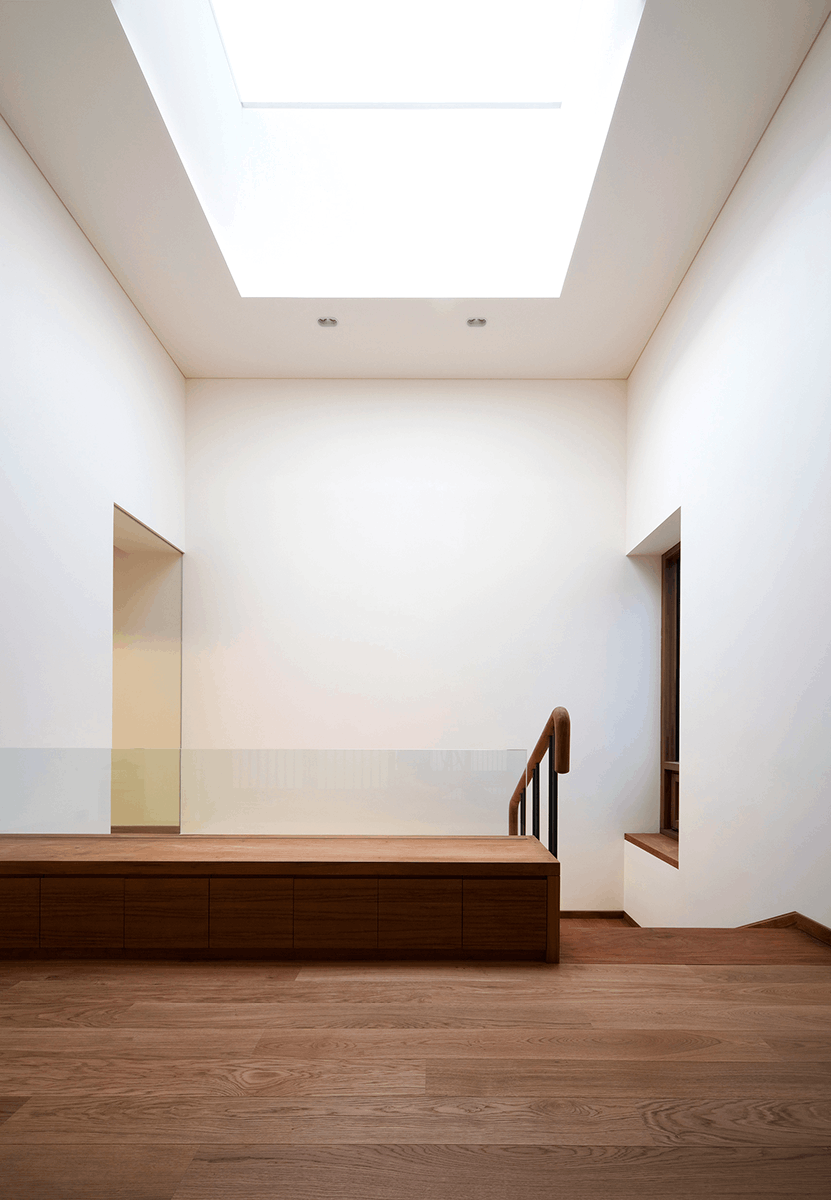 Foto eines Treppenaufgangs aus Holz und Glas mit Wänden die mit der Lehmfarbe I-PAINT in Dover-Weiß gestrichen wurden und von einem großen Skylight beleuchtet werden